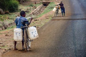 De Corvée ! témoigne de la détermination d'un enfant et d'un adulte poussant leurs vélos chargés de bidons.