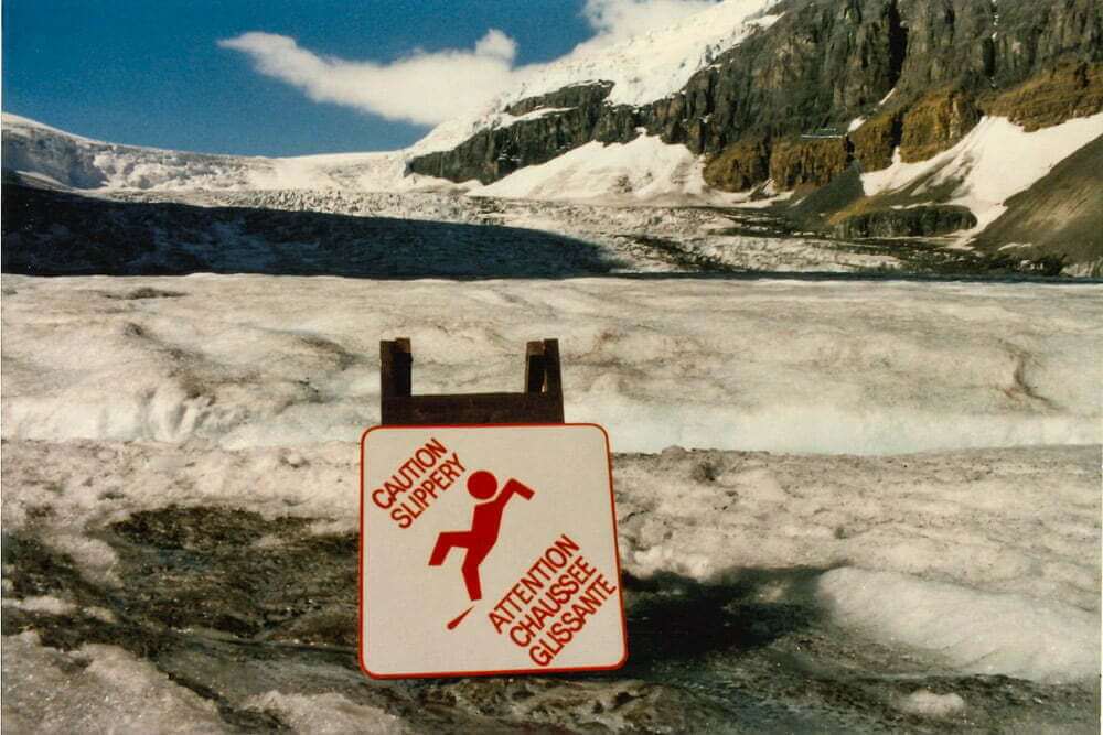 Pericoloso" offre une perspective humoristique sur la coexistence de l'homme et de la nature dans les Rocheuses canadiennes, mettant en scène un panneau d'avertissement sur une chaussée glissante devant un glacier massif.