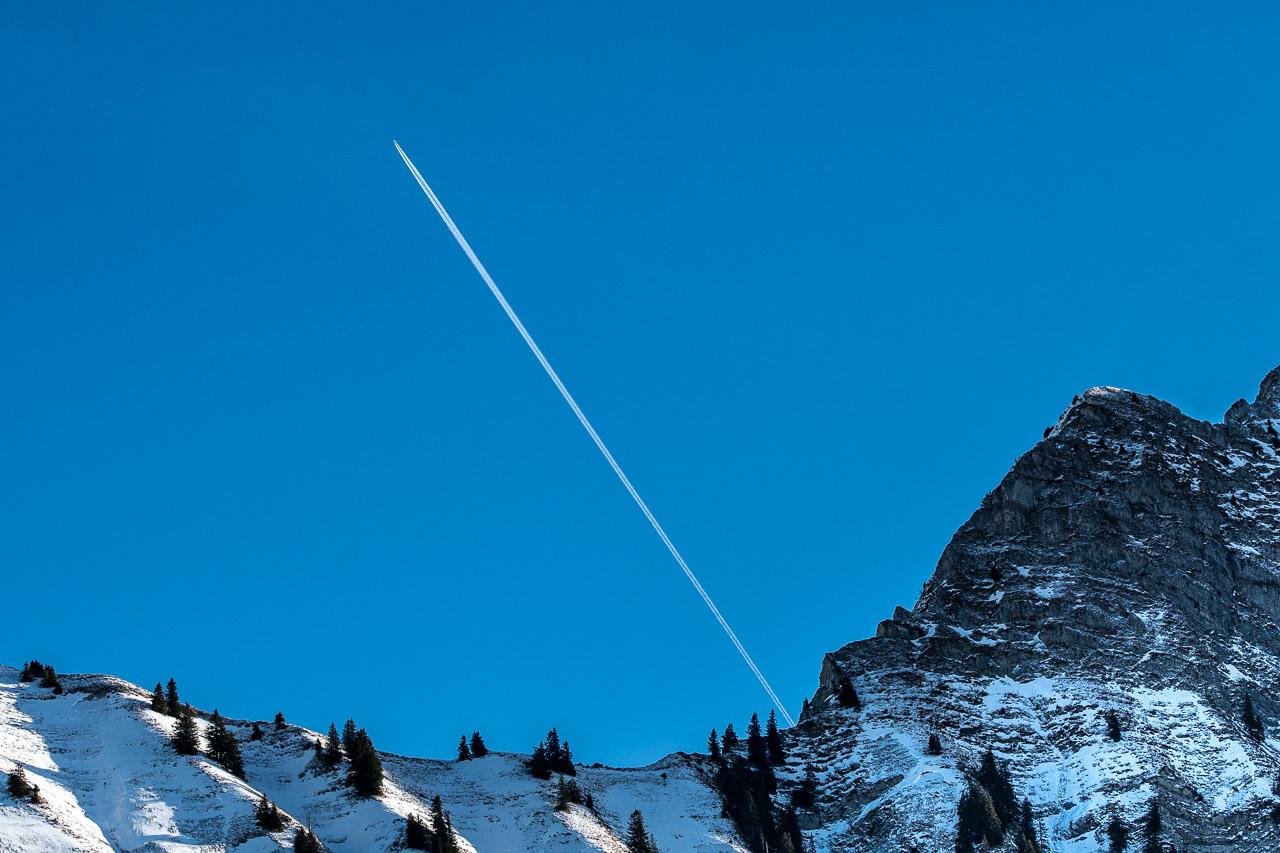 Évasion Alpestre illustre un moment unique capturé dans les Alpes suisses, où un avion s'échappe d'une montagne enneigée sous un ciel d'un bleu profond.