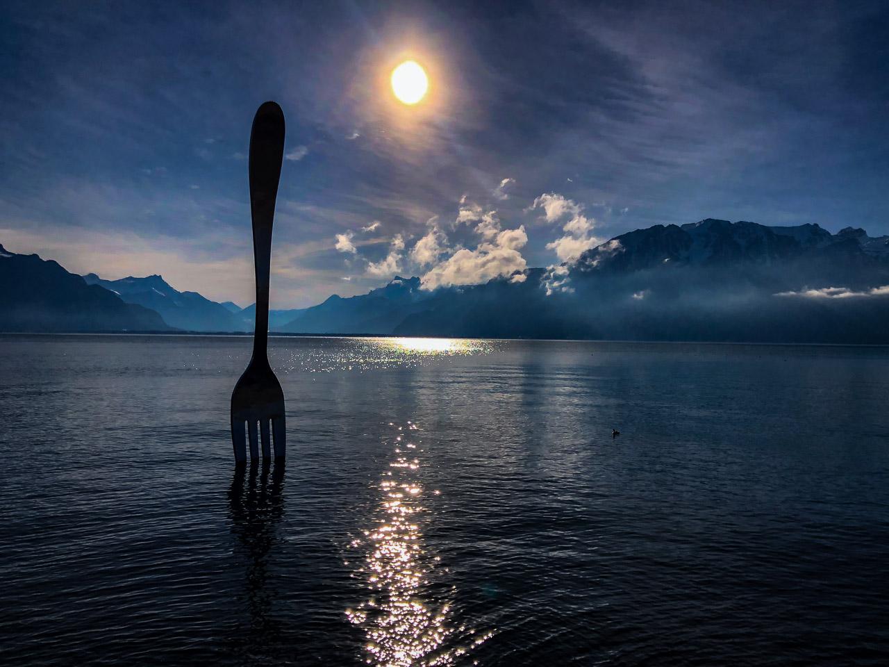 Cette photographie artistique, intitulée Dîner sur Léman, présente une scène captivante où une fourchette géante de 8 mètres se dresse audacieusement dans les eaux du lac Léman à Vevey.