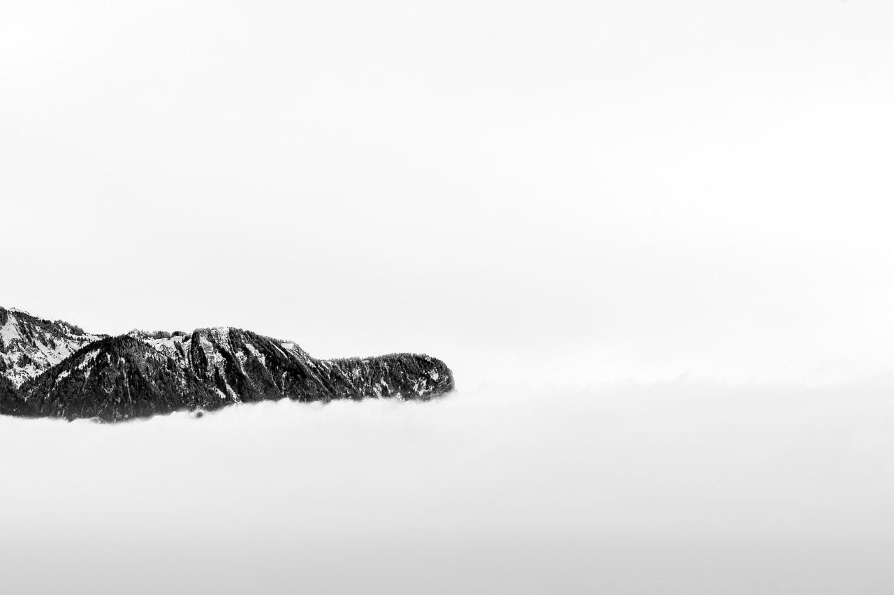 Sommet des Songes est une photographie noir et blanc qui capture la majesté des paysages suisses. Ce cliché révèle une montagne imposante surgissant d'une mer de nuages cotonneux, avec des contrastes saisissants entre les roches noires et le ciel d'un blanc pur.