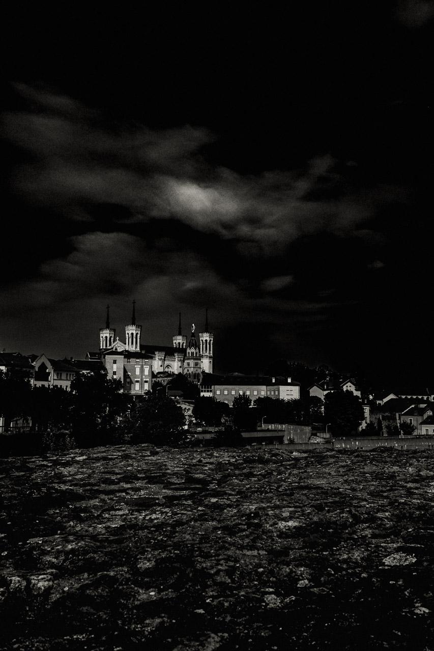 Le Phare des Ombres capture la basilique Notre Dame de Fourvière illuminée dans la pénombre, se détachant des ruines du Théâtre Romain de Lyon.